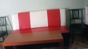 A room with a red and white sofa, a wooden coffee table, and two black chairs. - Eagles Lodge (Naivasha)