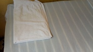 A bed with a white striped sheet and a folded white towel on it. - Eagles Lodge (Naivasha)