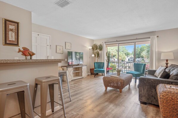 A living room with a sofa, a television, and a balcony with chairs.