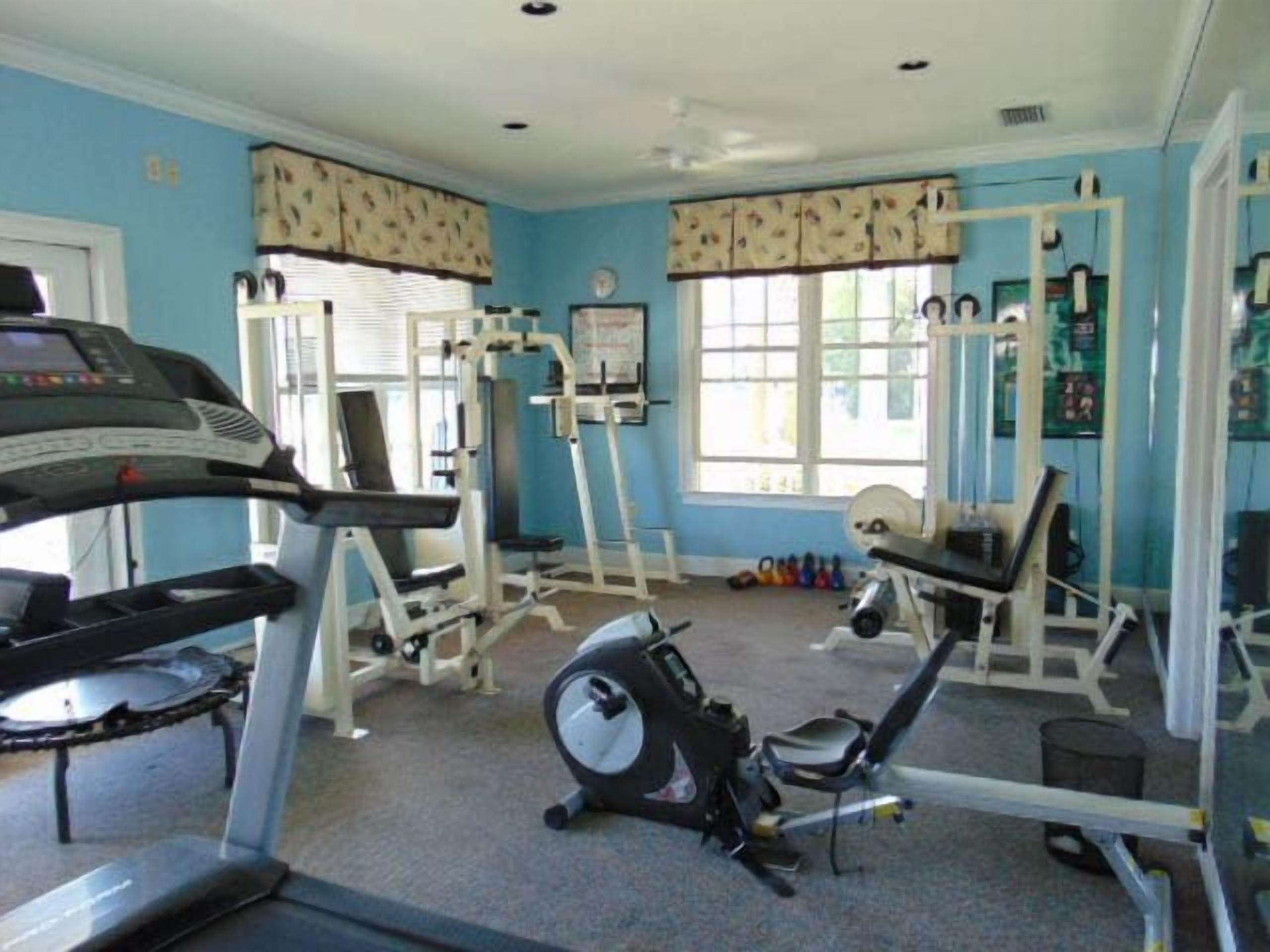 Une salle de sport équipée de machines de cardio, d’appareils de musculation et dotée d’une fenêtre avec des stores.