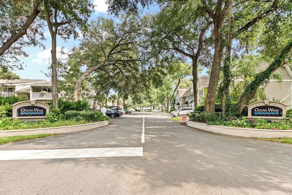 Une rue résidentielle bordée de maisons portant l’inscription « Ocean Walk », entourée d’arbres et de verdure.