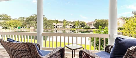 A covered outdoor area with wicker furniture and a view of a body of water and buildings in the background.