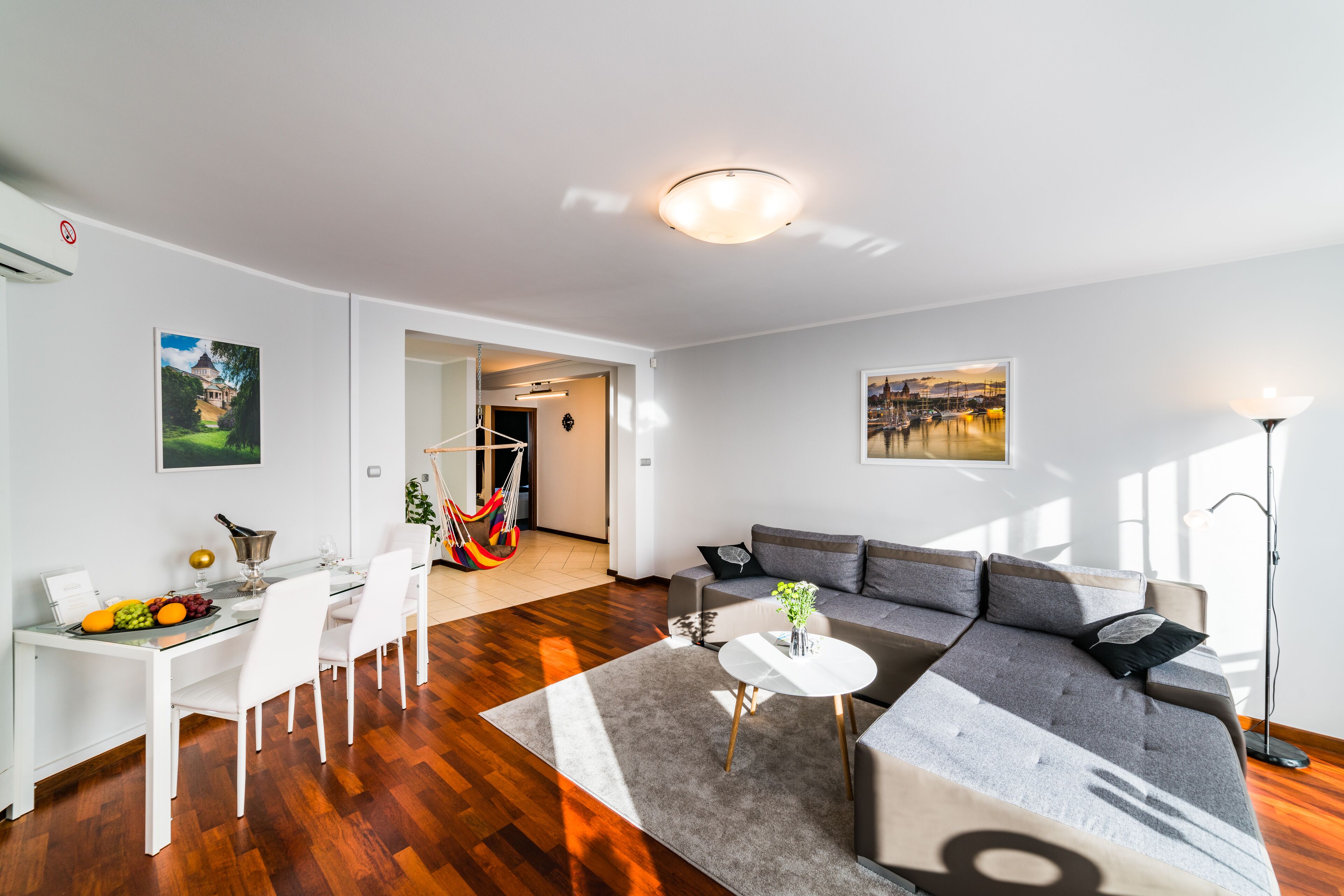 Ett modernt vardagsrum med en soffa, ett matbord med stolar, ett soffbord och en matta. Det finns en tavla på väggen och en lampa på en av sidoborden.