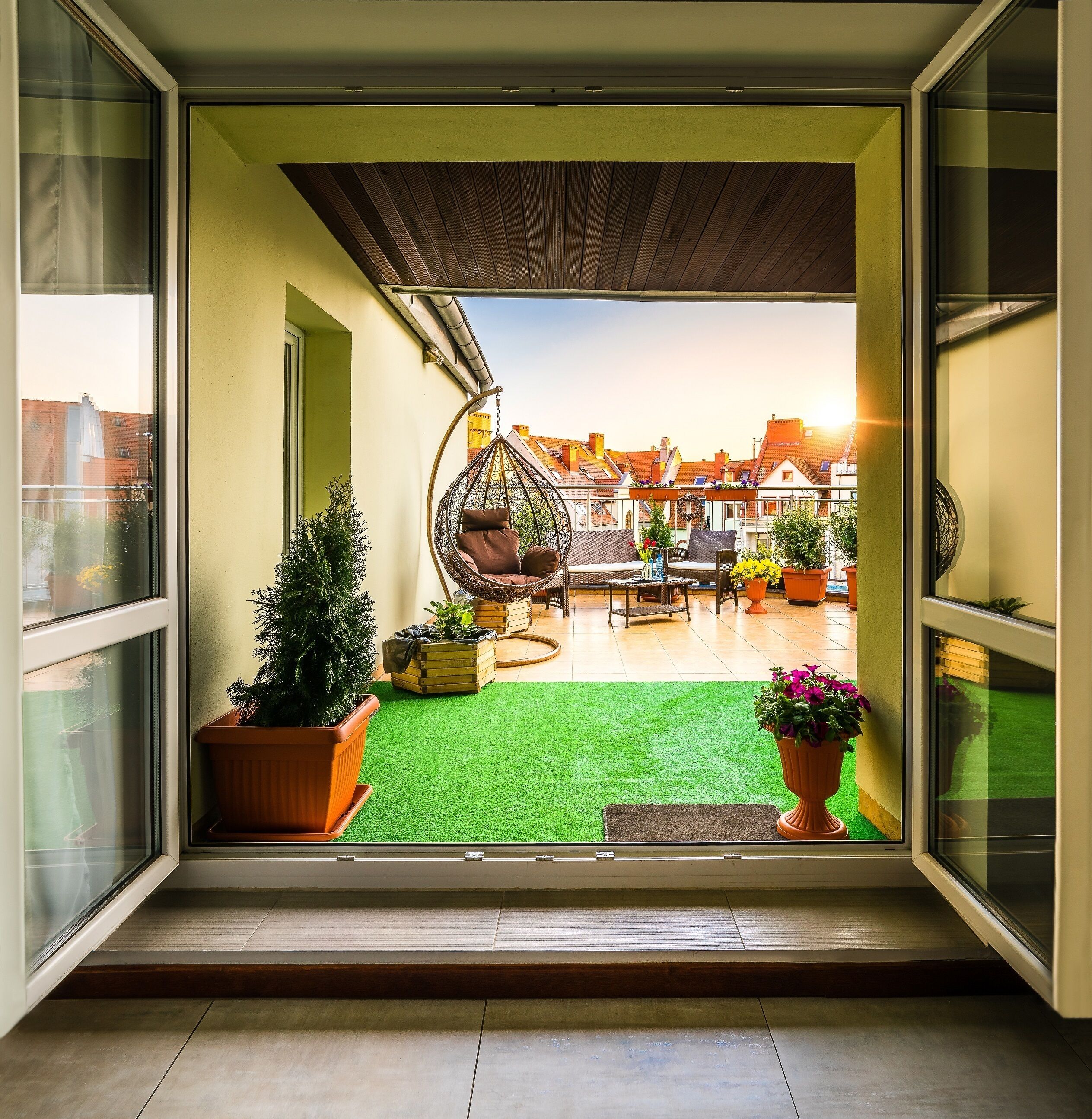 A balcony with a hanging chair, potted plants, and a view of buildings in the background.