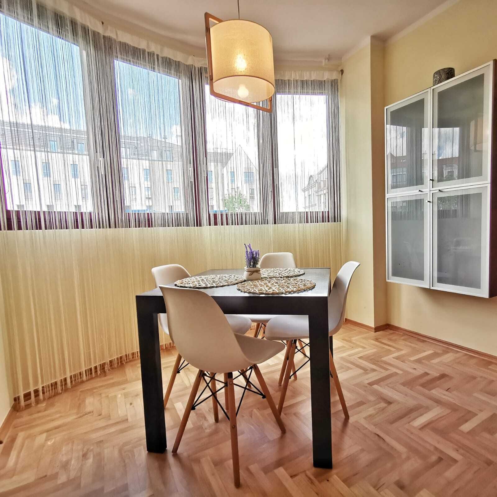 Comedor con mesa, sillas, lámpara colgante y ventana con cortinas.