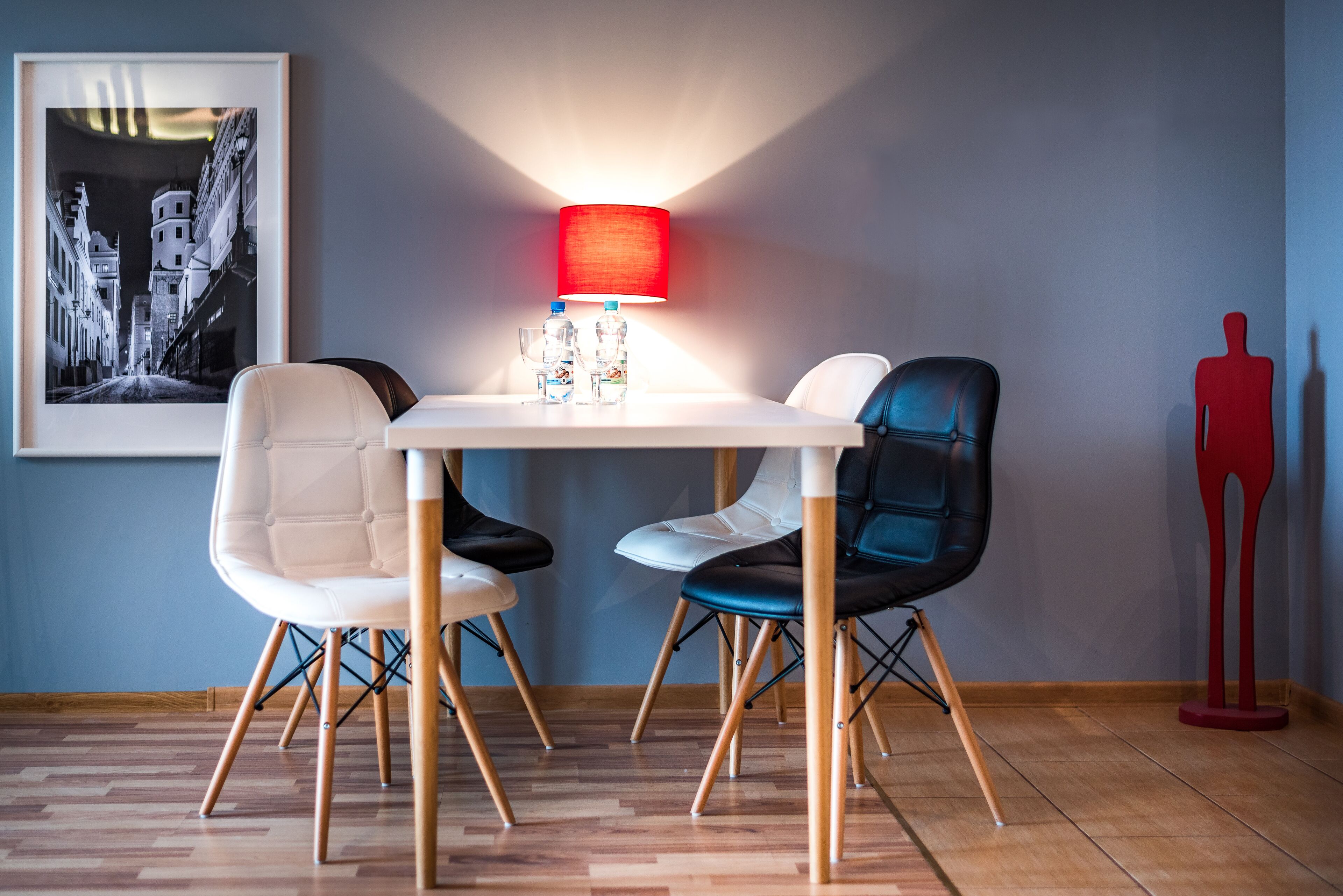 Un comedor con una mesa, sillas, una lámpara roja, un cuadro enmarcado y una escultura roja.