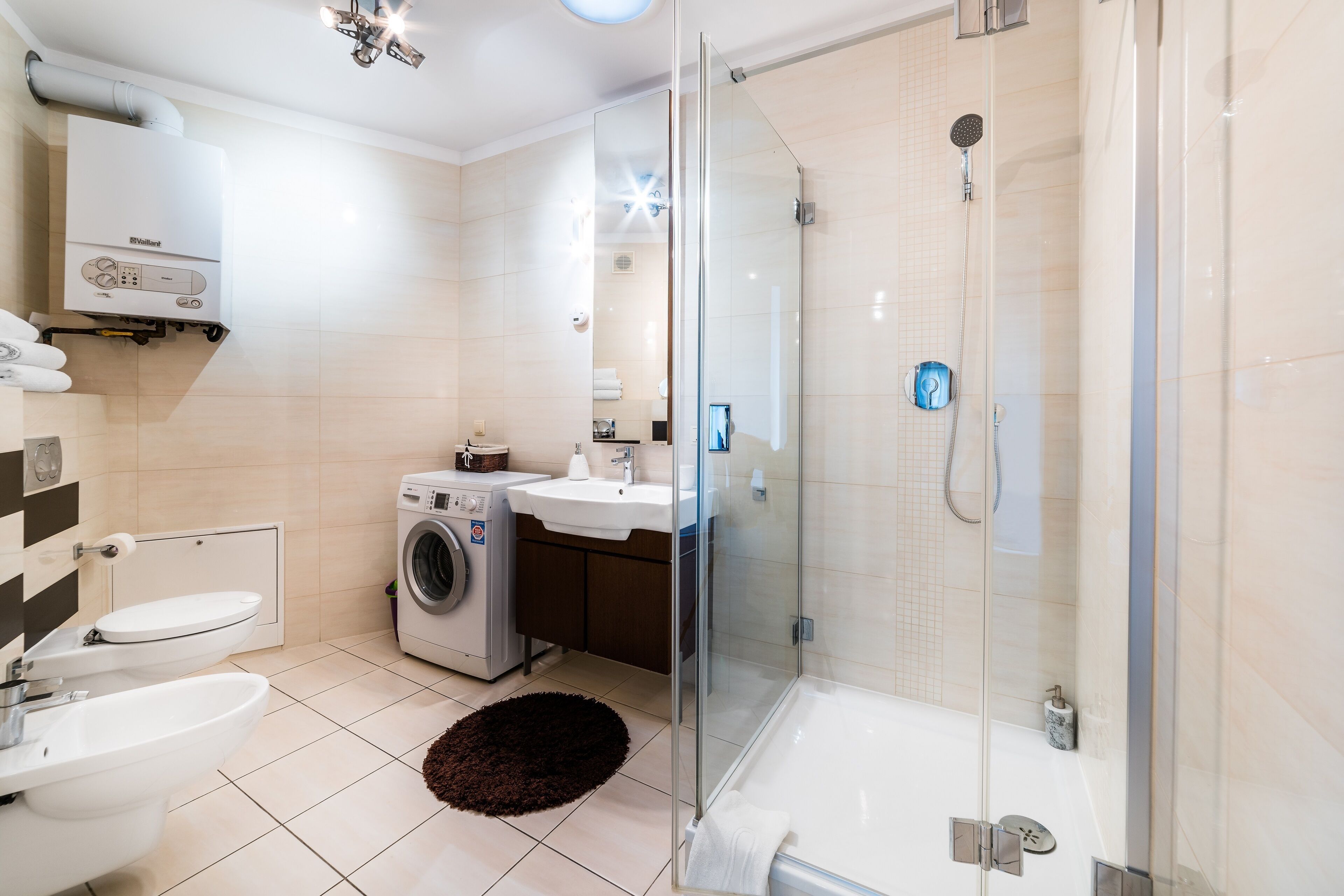 A modern bathroom with a glass-enclosed shower, a built-in washing machine, and a sink.