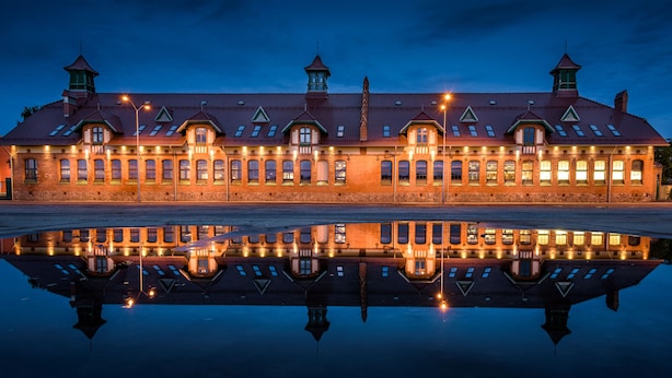 Een groot, historisch gebouw met meerdere ramen en een centrale toren, weerspiegeld in een rustig waterlichaam.