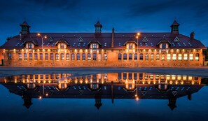 A large, historic building with multiple windows and a central tower, reflecting in a calm body of water.