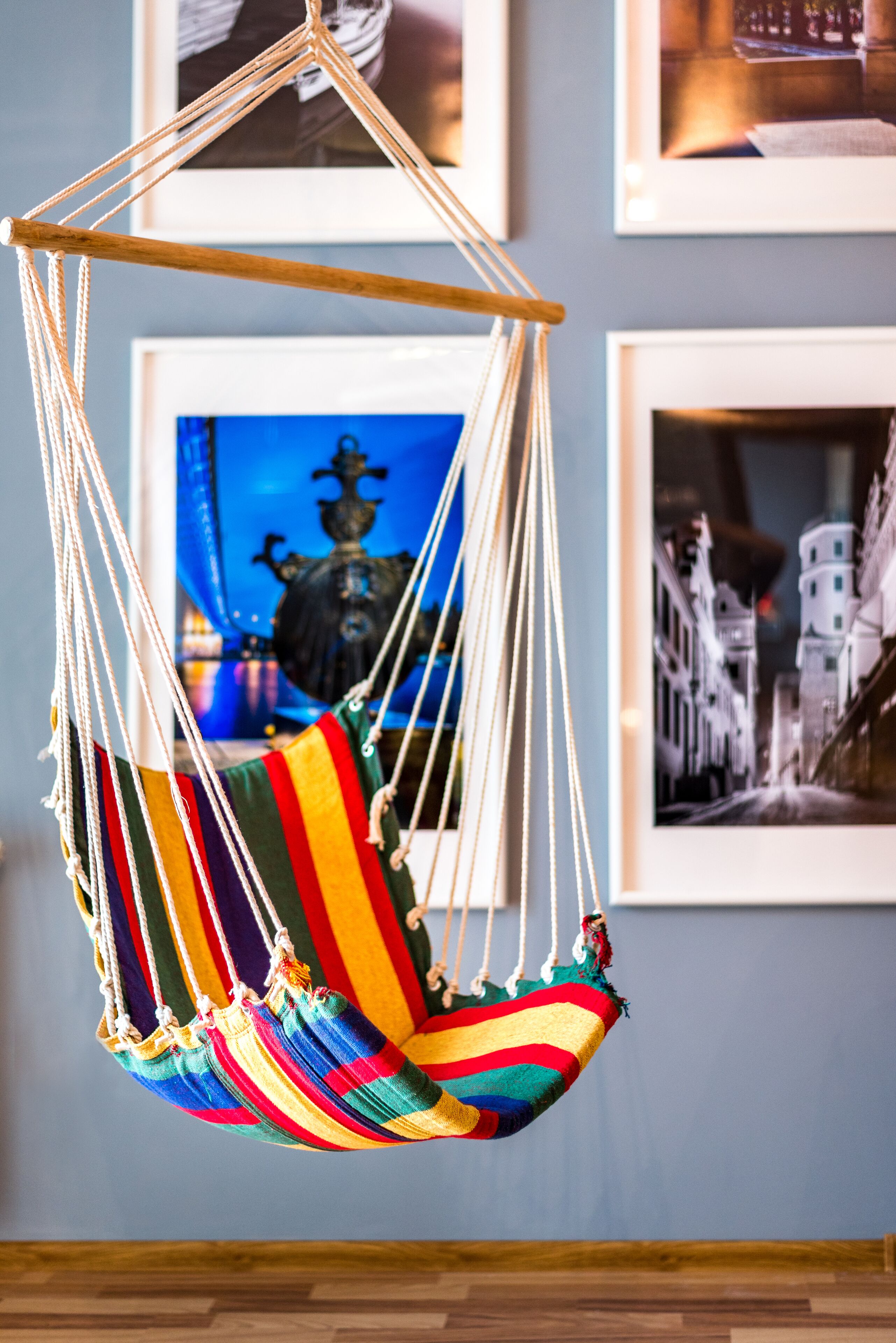 A colorful hanging chair suspended from the ceiling in a room with framed pictures on the wall.