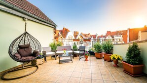 Een terras met rieten meubels, een hangstoel en potplanten.