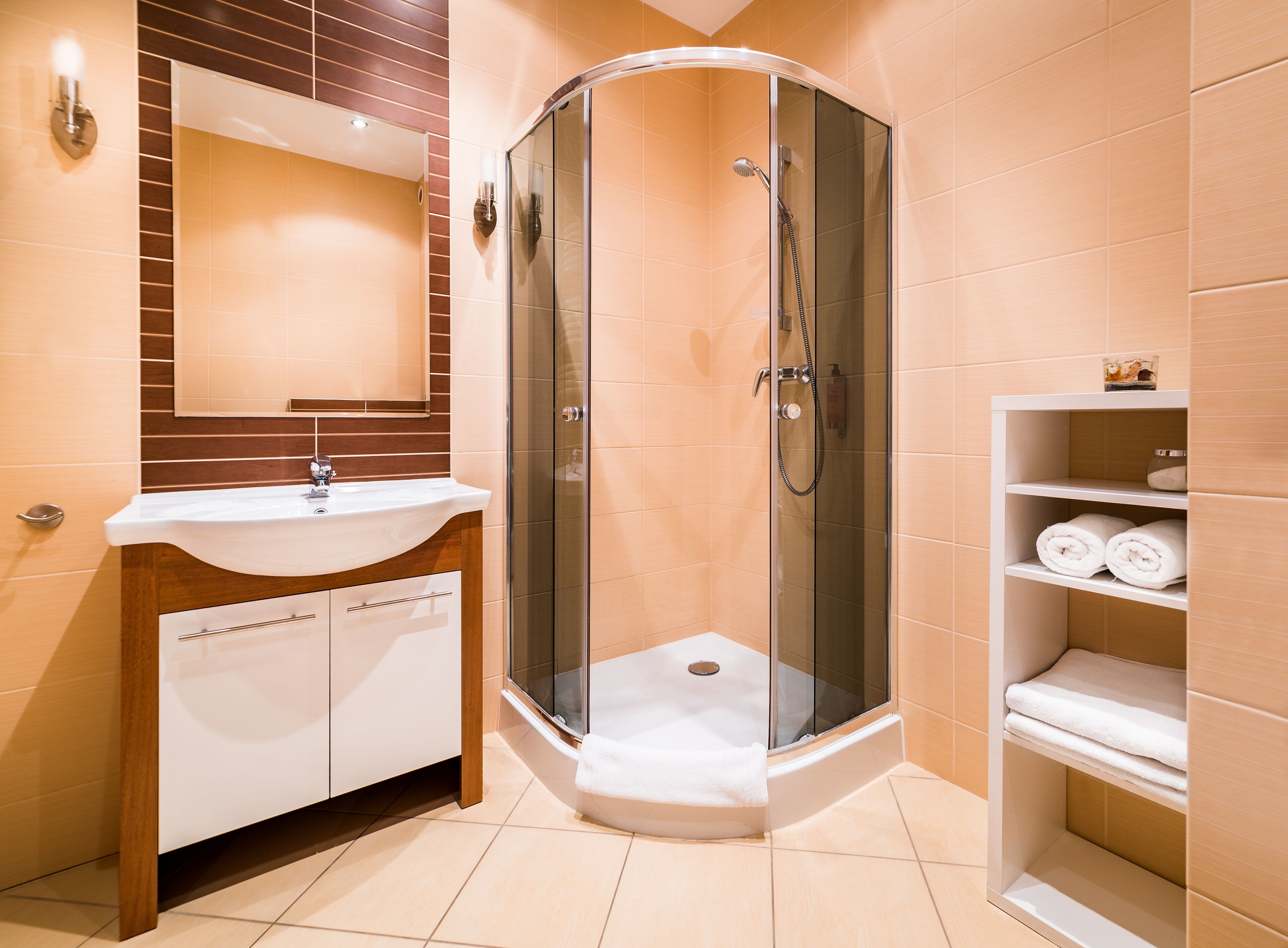 Un bagno moderno con doccia vetrata, lavandino bianco e mobile vanitario in legno.