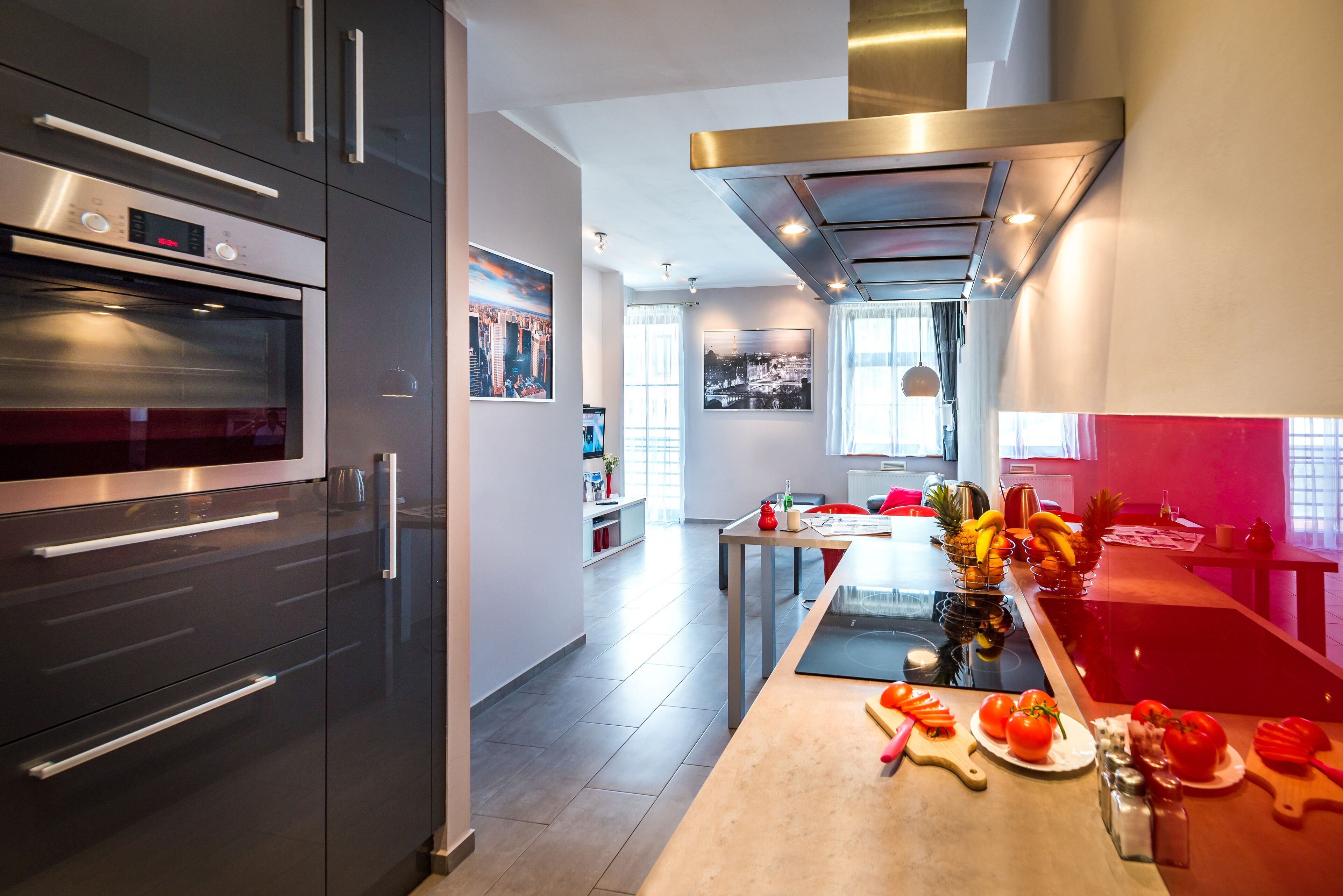 A modern kitchen with stainless steel appliances, a central island with fruits and vegetables, and a dining area with a table and chairs.