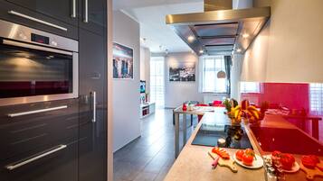 Una cocina moderna con electrodomésticos de acero inoxidable, una isla central con frutas y verduras, y un comedor con una mesa y sillas.