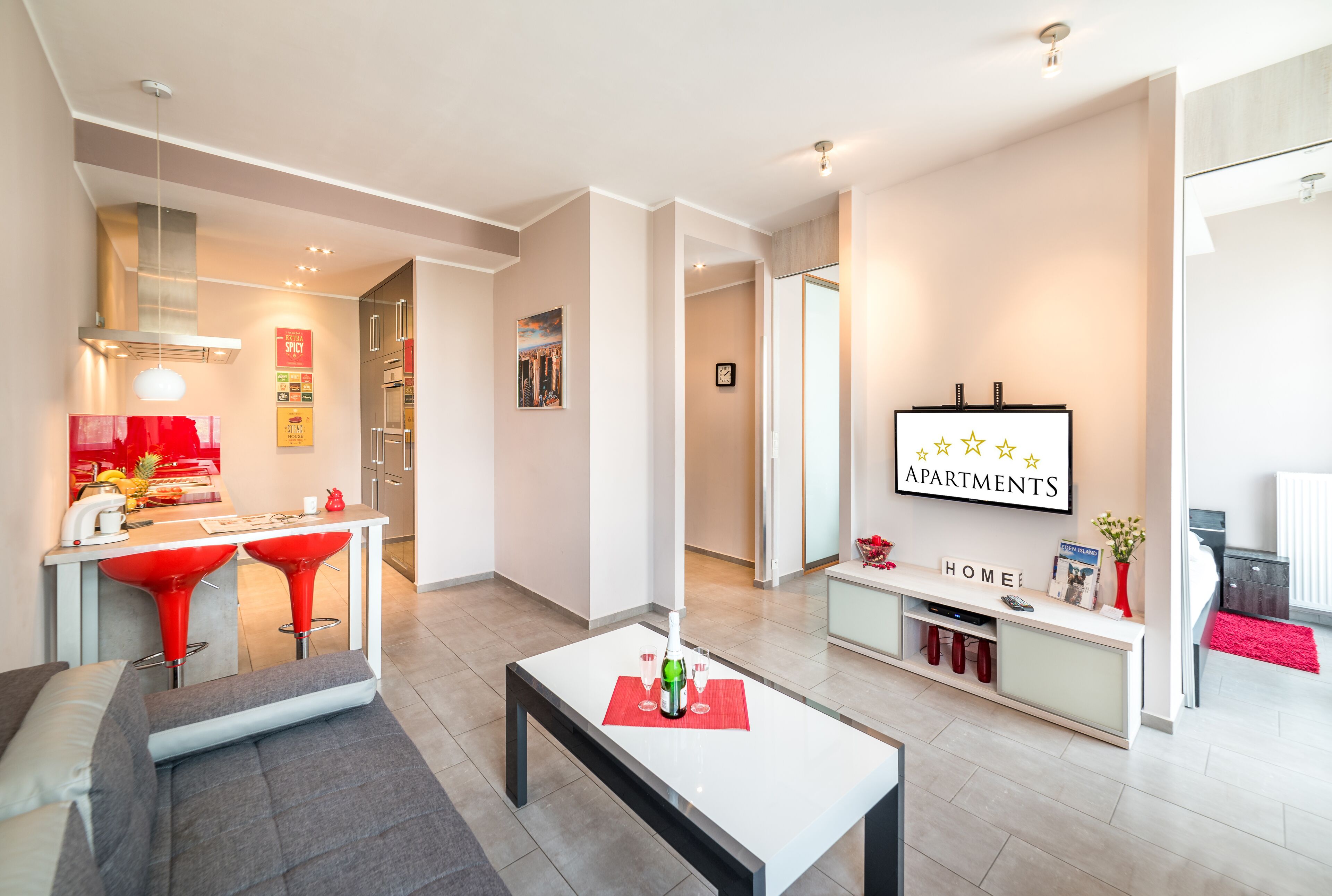A modern living room with a dining area, a kitchen, and a TV displaying 'APARTMENTS'.