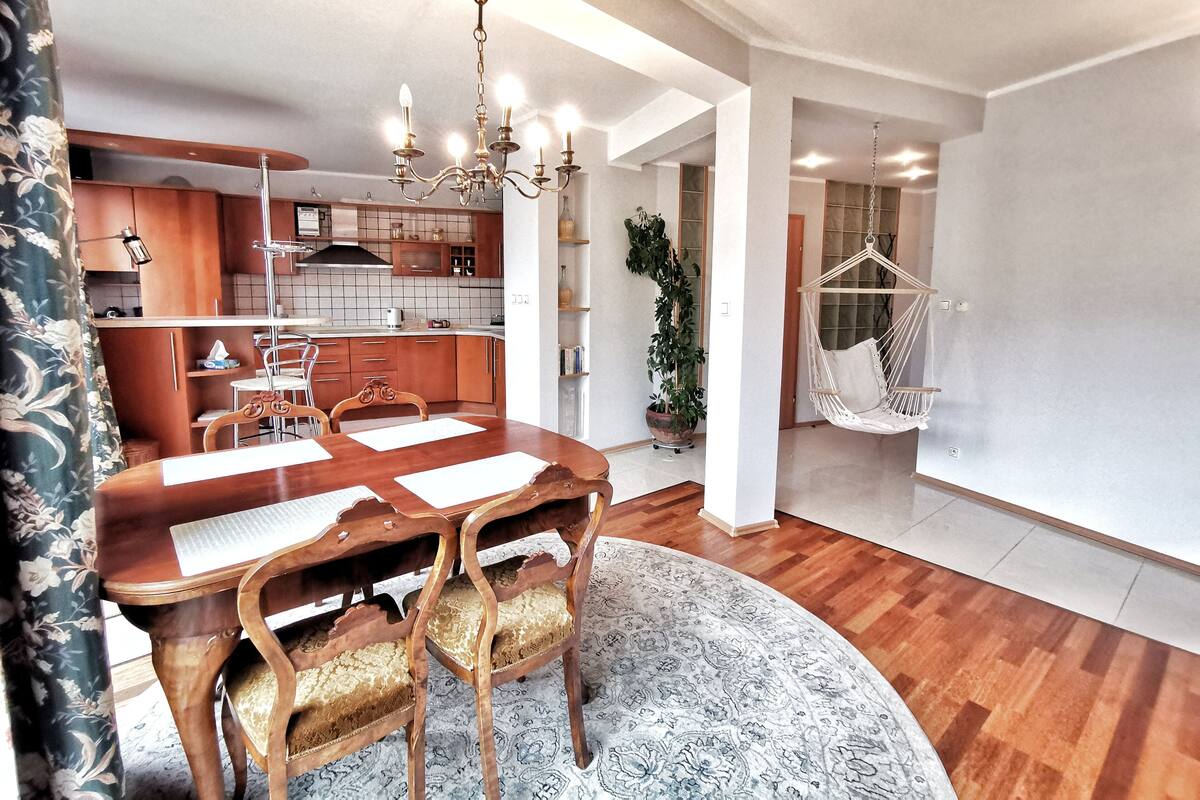 Une cuisine moderne avec des meubles en bois, une table à manger avec des chaises, un lustre et un fauteuil suspendu.