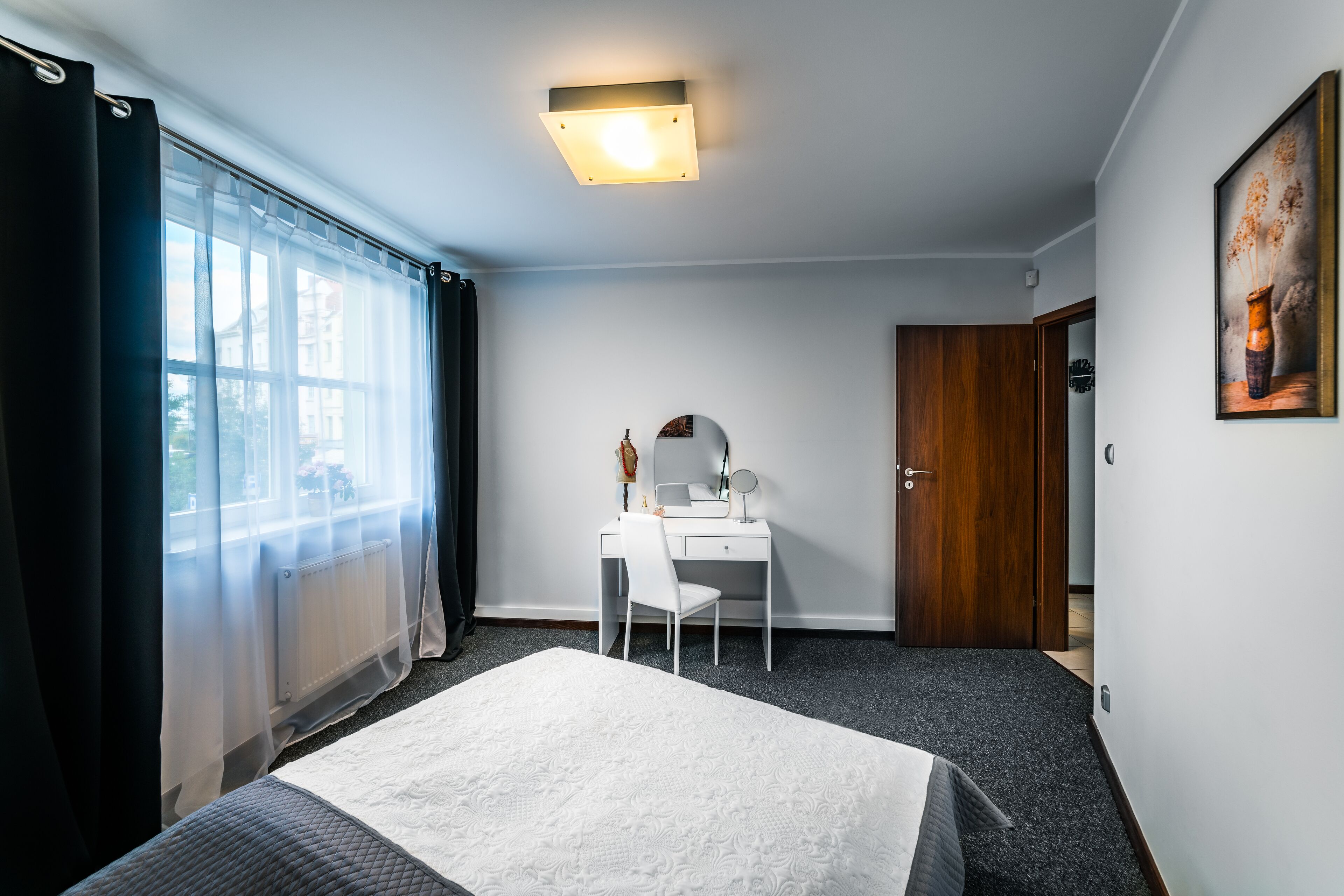 A hotel room with a bed, a desk with a chair, a mirror, and a door.