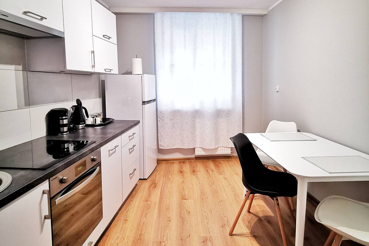 Une cuisine moderne avec des armoires blanches, un comptoir noir et un plancher en bois. On y trouve un coin repas avec une table blanche et des chaises noires.