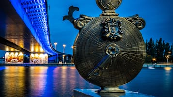 A large, ornate metal sculpture with a globe and compass design, labeled "astrolabum," placed on a concrete pedestal by a waterfront.