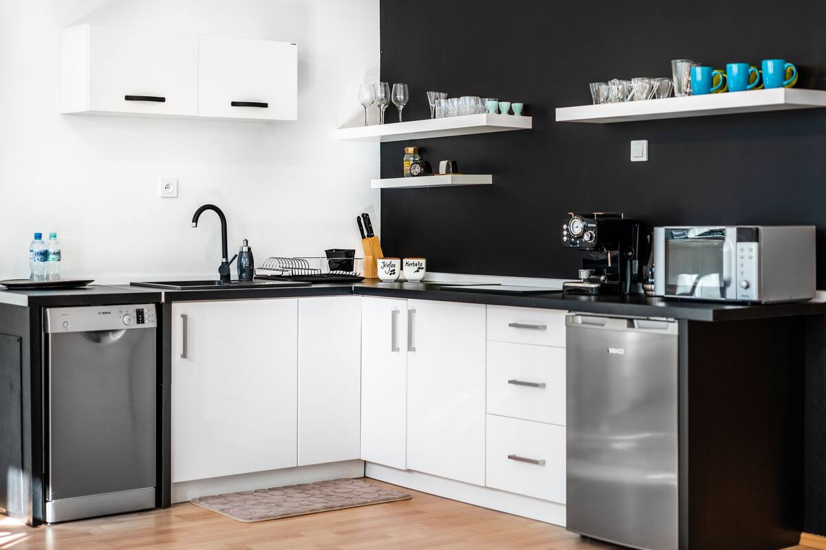 Une cuisine moderne avec des meubles blancs, un plan de travail noir, un lave-vaisselle, une machine à café et un four à micro-ondes.