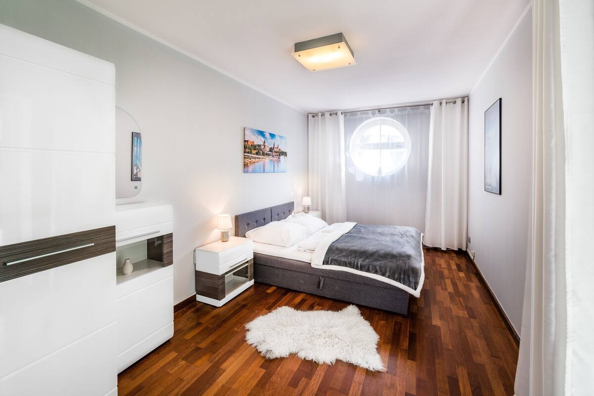 Une chambre moderne avec un lit, une table de chevet, une lampe et une vue sur le paysage urbain par la fenêtre.