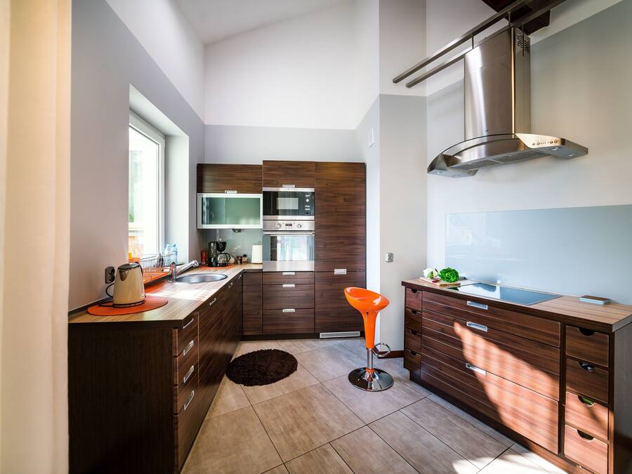 A modern kitchen with dark wooden cabinets, stainless steel appliances, and a large window providing natural light.