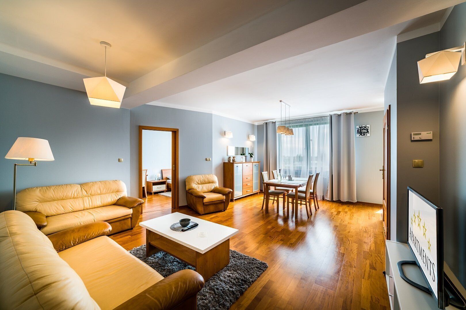 A modern living room with a sofa, armchairs, a coffee table, and a dining area with a table and chairs.