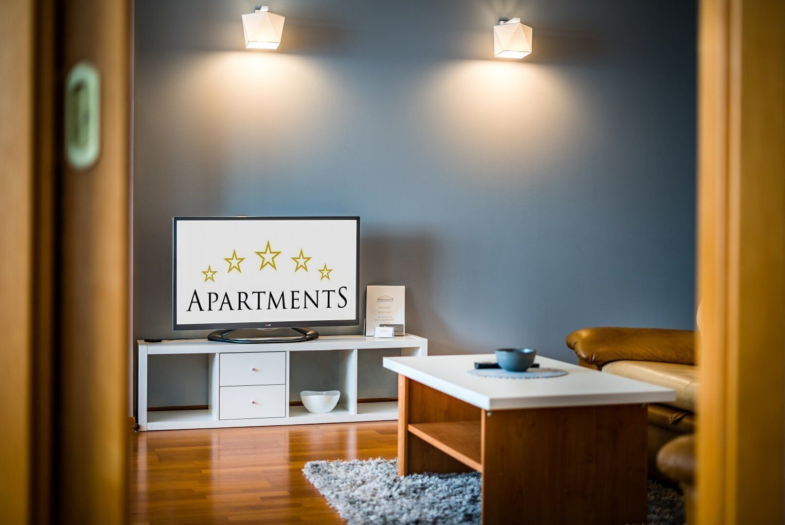 Ein modernes Wohnzimmer mit Flachbildfernseher, Couchtisch, Sofa und einer Wandleuchte.