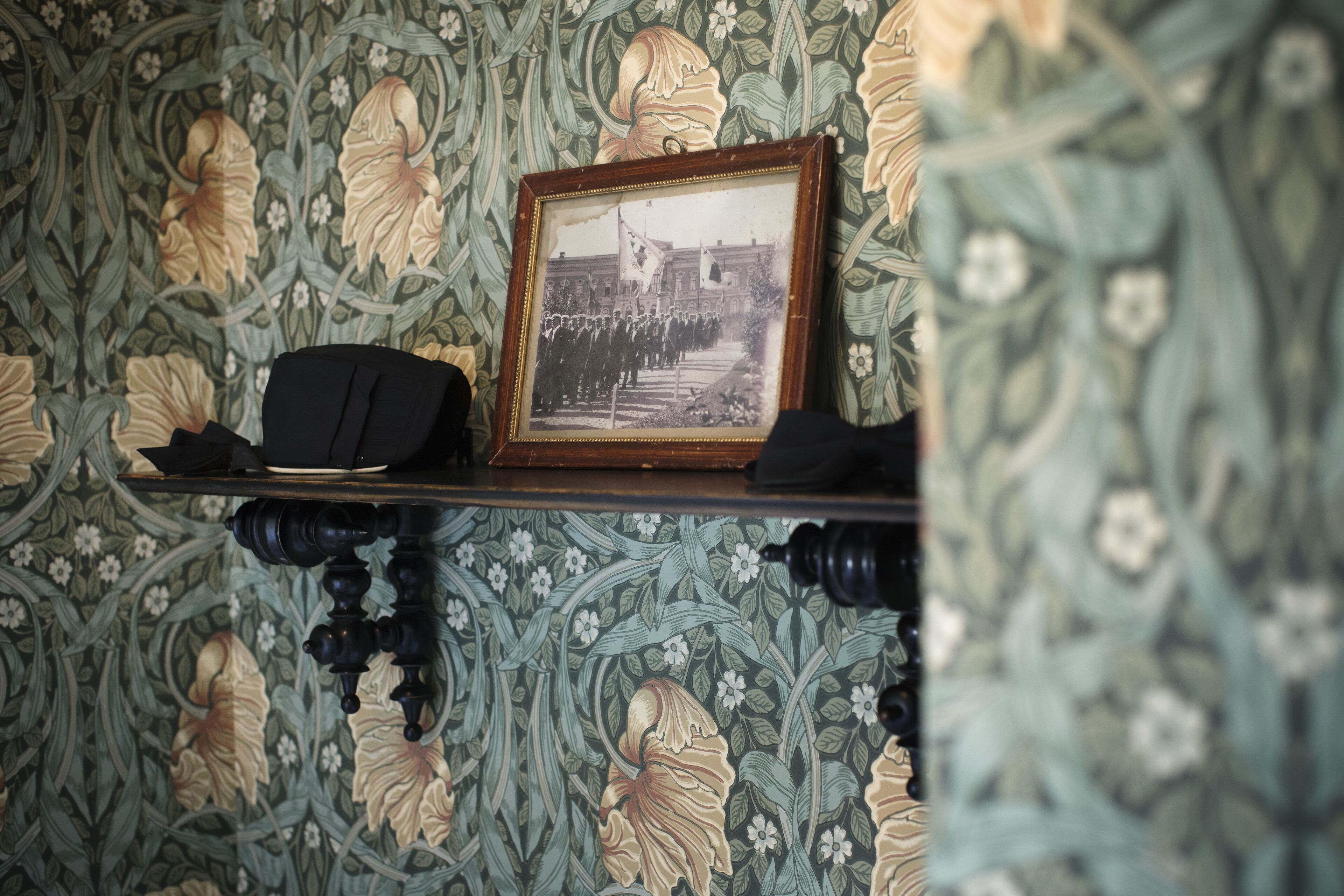A framed photograph on a shelf against a floral wallpaper background.
