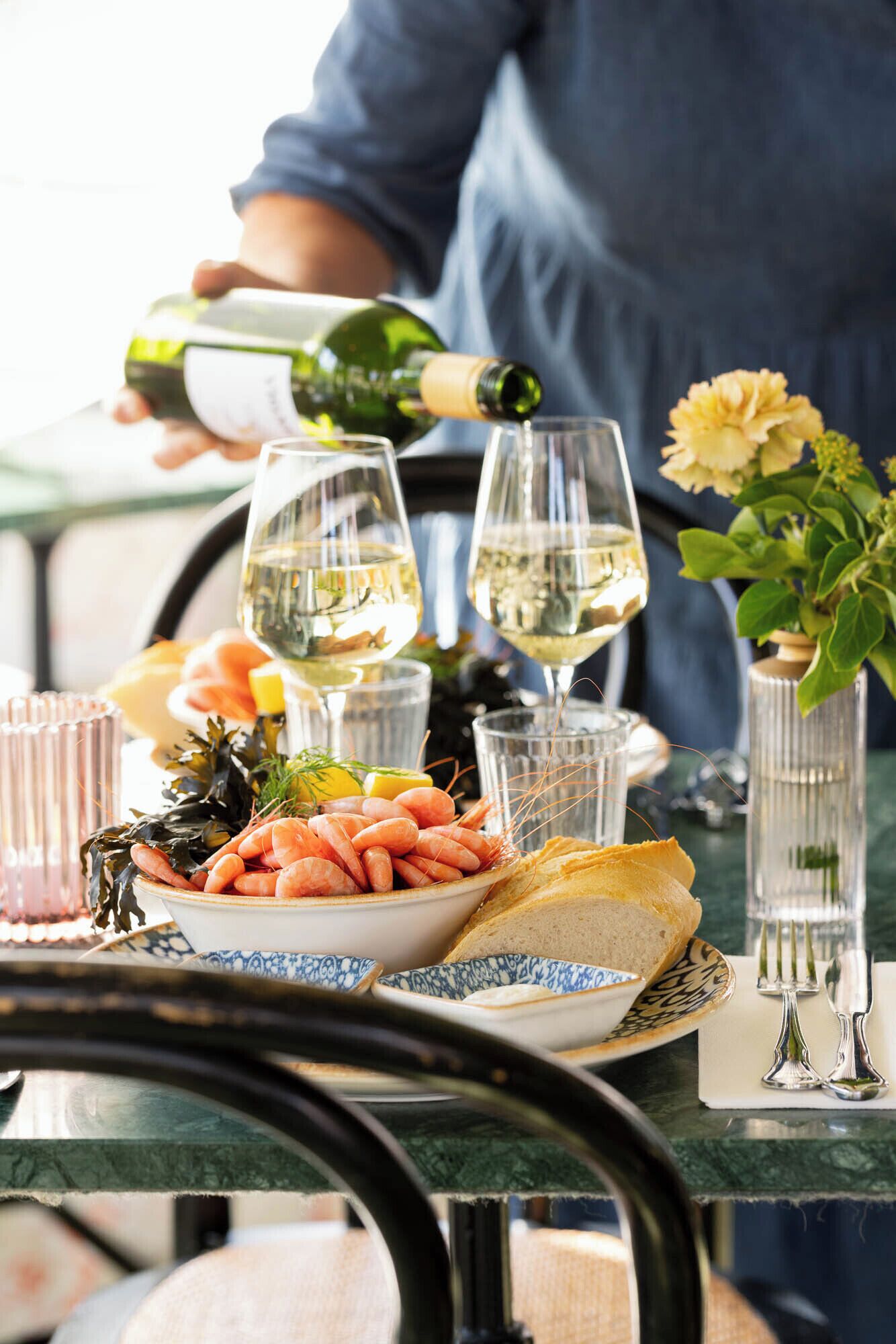 A table set with seafood, bread, and glasses of white wine, with a person pouring wine.