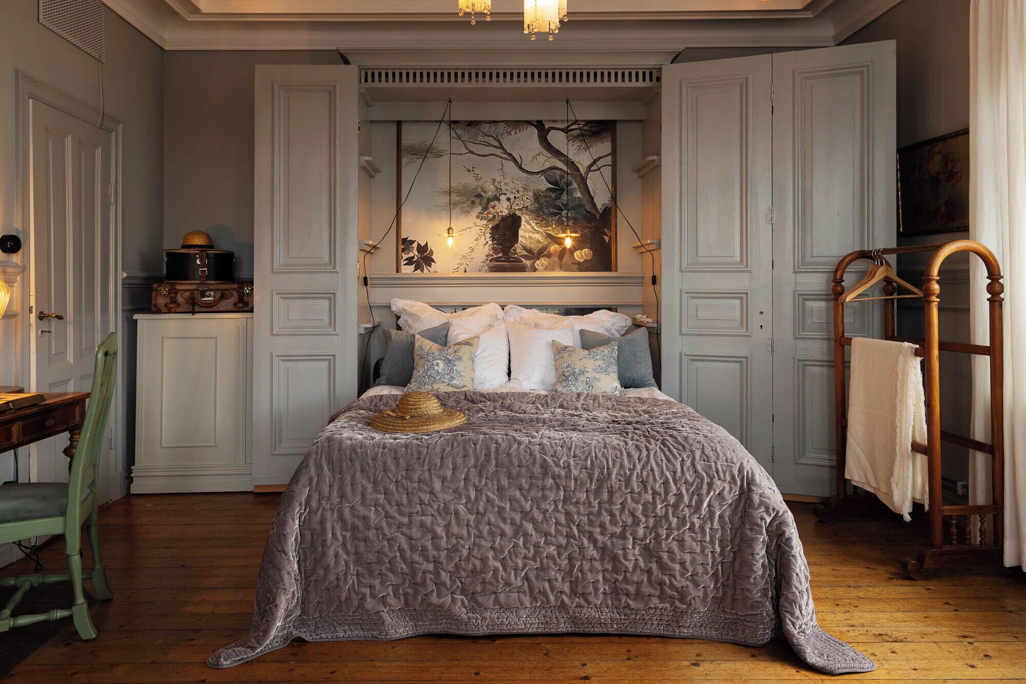 Un dormitorio con una cama grande, una silla de madera, un aparador y un cuadro en la pared.