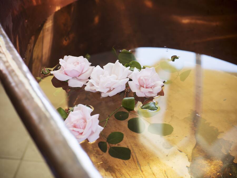 A copper bathtub with pink roses floating in water.