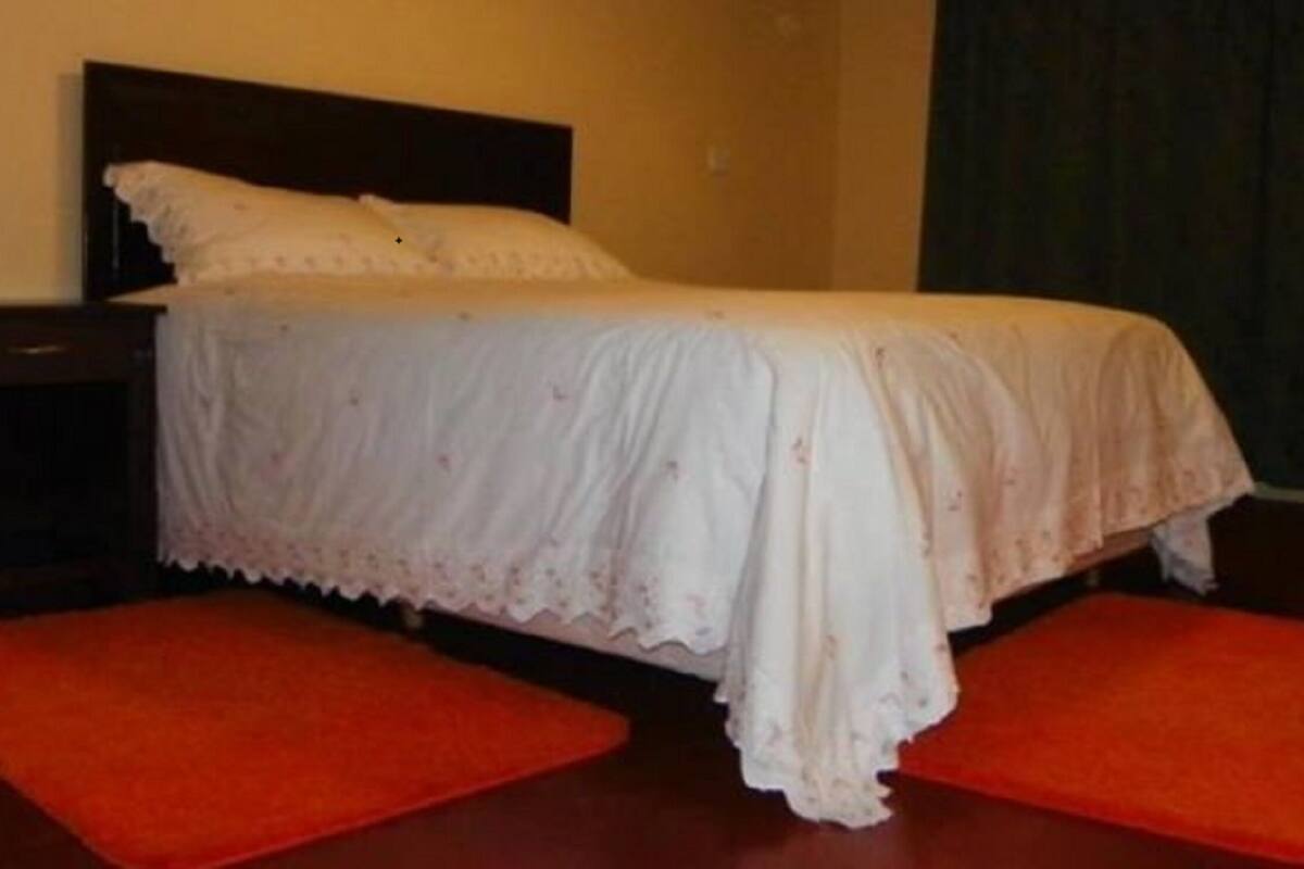 A bed with a white bedspread and pillows, flanked by two red rugs on a wooden floor.