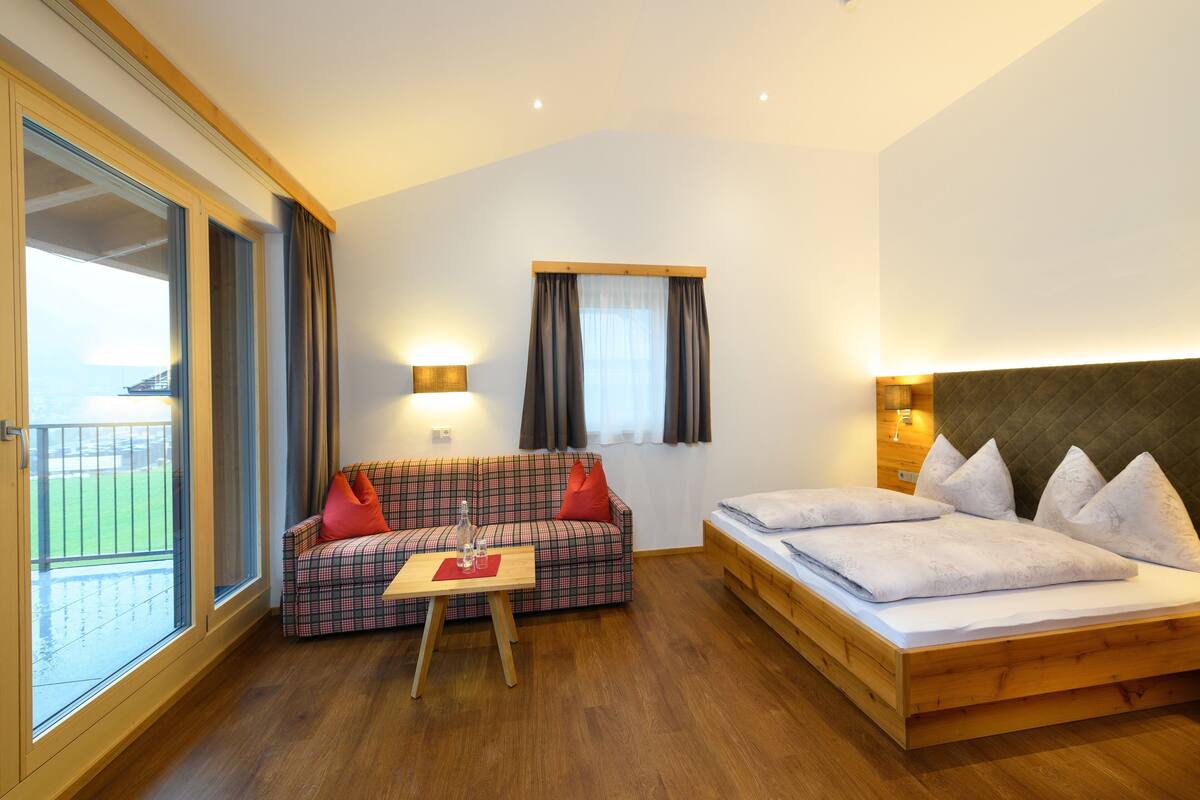 Um quarto com cama, sofá, mesa e janela com cortinas.
