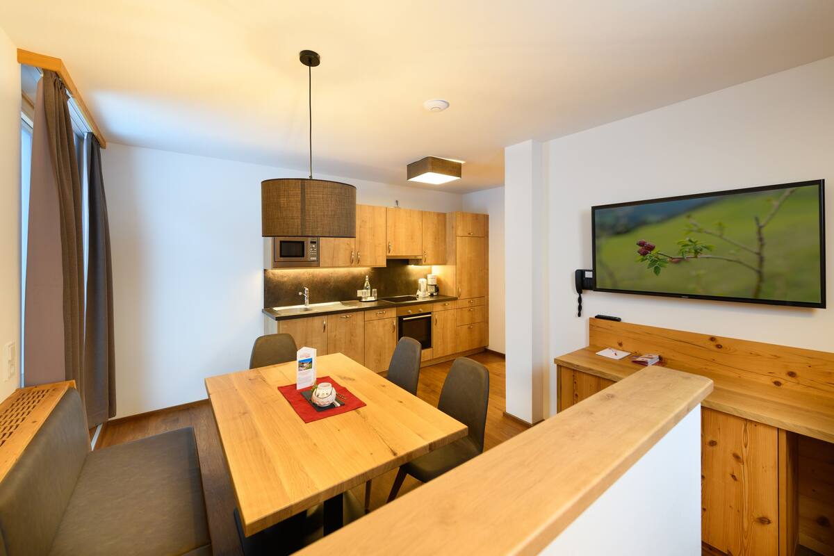 Cozinha moderna com armários de madeira, uma mesa de jantar e uma TV fixada na parede.