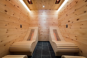 Una sauna con paredes y bancos de madera, que cuenta con un elemento calefactor central y un suelo de baldosas.