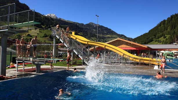A swimming pool with a water slide, surrounded by mountains and a clear sky. - Appartement-Pension Kendlbacher (Grossarl)