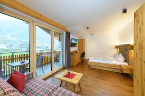 A modern room with a large sliding glass door leading to an outdoor area, a wooden bed, a small table, and a sofa with plaid upholstery.