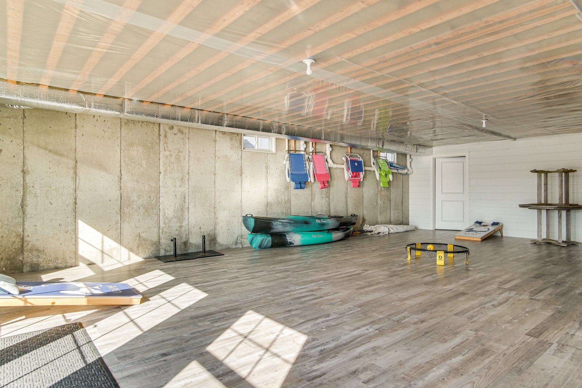 A spacious room with a high ceiling, concrete walls, and a wooden floor. There are kayaks and a paddleboard in the room.