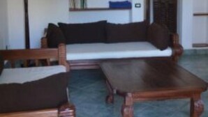 A living room with a sofa, two armchairs, a coffee table, a floor lamp, and a bookshelf. - Girasoli Hotel (Malindi)