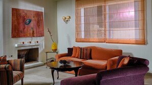 A living room with a sofa, armchairs, a coffee table, a fireplace, and a large window with blinds. - Villa Helios with private pool, beautiful sea view and sunny terrace (Agios Nikolaos Lassithi)
