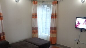 A living room with a sofa, ottoman, and a coffee table. There is a television mounted on the wall.