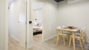 Una habitación moderna y minimalista con una mesa y sillas de madera, una cama con ropa de cama estampada y un equipo de aire acondicionado en la pared.