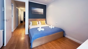 A modern hotel room with a wooden floor, a bed with a blue bedspread, and a painting on the wall. - Stay U-nique Apartment Travessera (Barcelona)