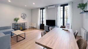 A modern living room with a long wooden table, a sofa, a TV, and a plant. - Stay U-nique Apartment Travessera (Barcelona)