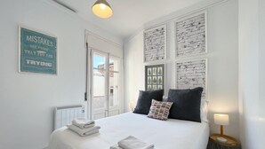 Ein Schlafzimmer mit einem Bett, zwei Kissen, einem Nachttisch mit Lampe, einem Heizkörper und einer Wand mit gerahmten Bildern.
