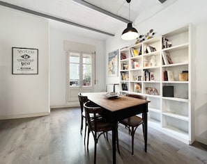 Een eetgedeelte met een houten tafel en stoelen, een boekenkast vol boeken en decoratieve objecten, en een ingelijst motiverend citaat aan de muur.