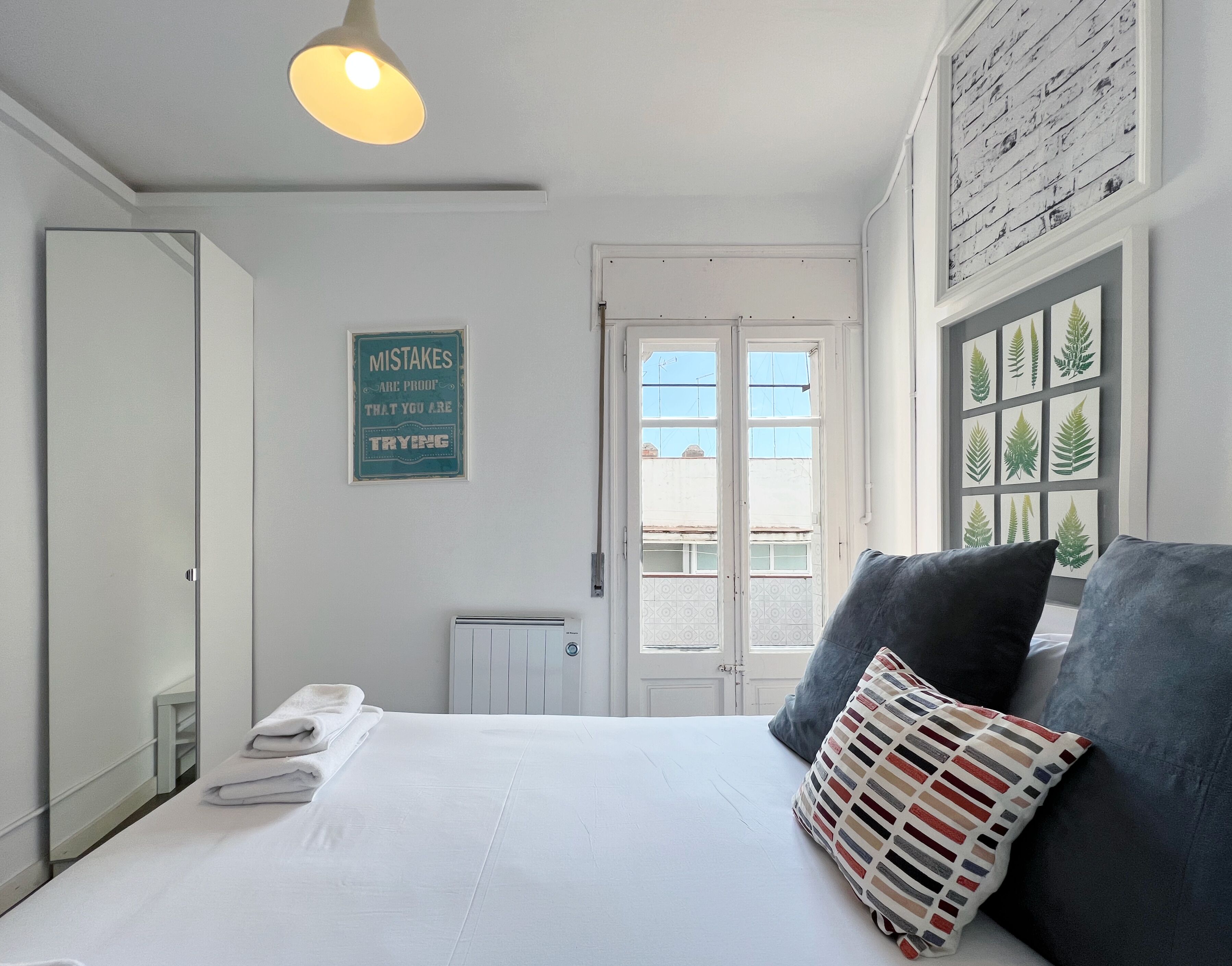 Une chambre à coucher avec un lit, des oreillers, un radiateur, une porte et un mur orné d’une affiche.