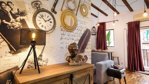 Ein Zimmer mit einem hölzernen Schreibtisch, einer Lampe, einem Büstenporträt und einer Wand, die mit Antiquitäten und Schriftstücken geschmückt ist.