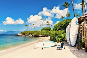 A beach with surfboards, a paddleboard, and a chair.